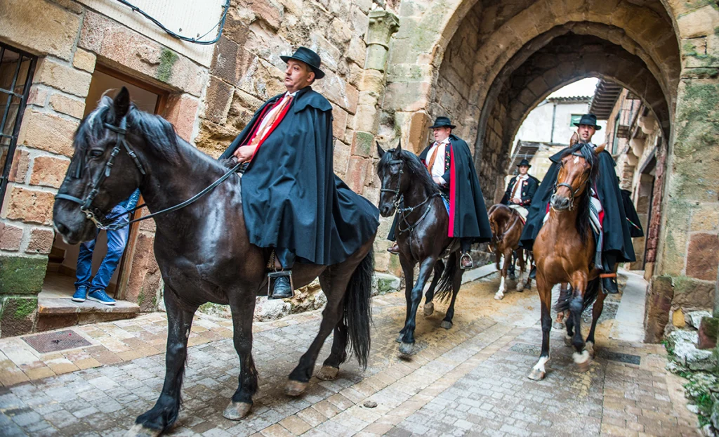 hombres a caballo vestidos con capas bajando por los arcos de Atienza